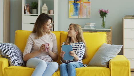 Mujer-Rubia-Sosteniendo-Una-Taza-De-Café-Y-Hablando-Con-Su-Hija-Adolescente-Que-Sostiene-Una-Tableta-1