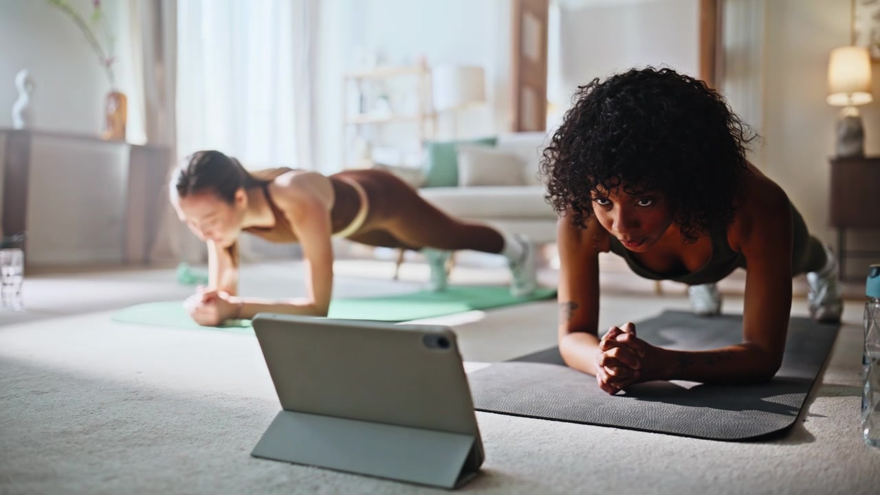 Athletic women holding plank following tablet workout home. Fitness training.