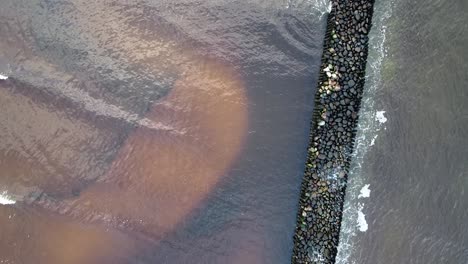 aerial birdseye view of old breakwater - stone pier at pape beach baltic sea, latvia, cloudy and calm day, wide angle establishing drone shot moving backwards