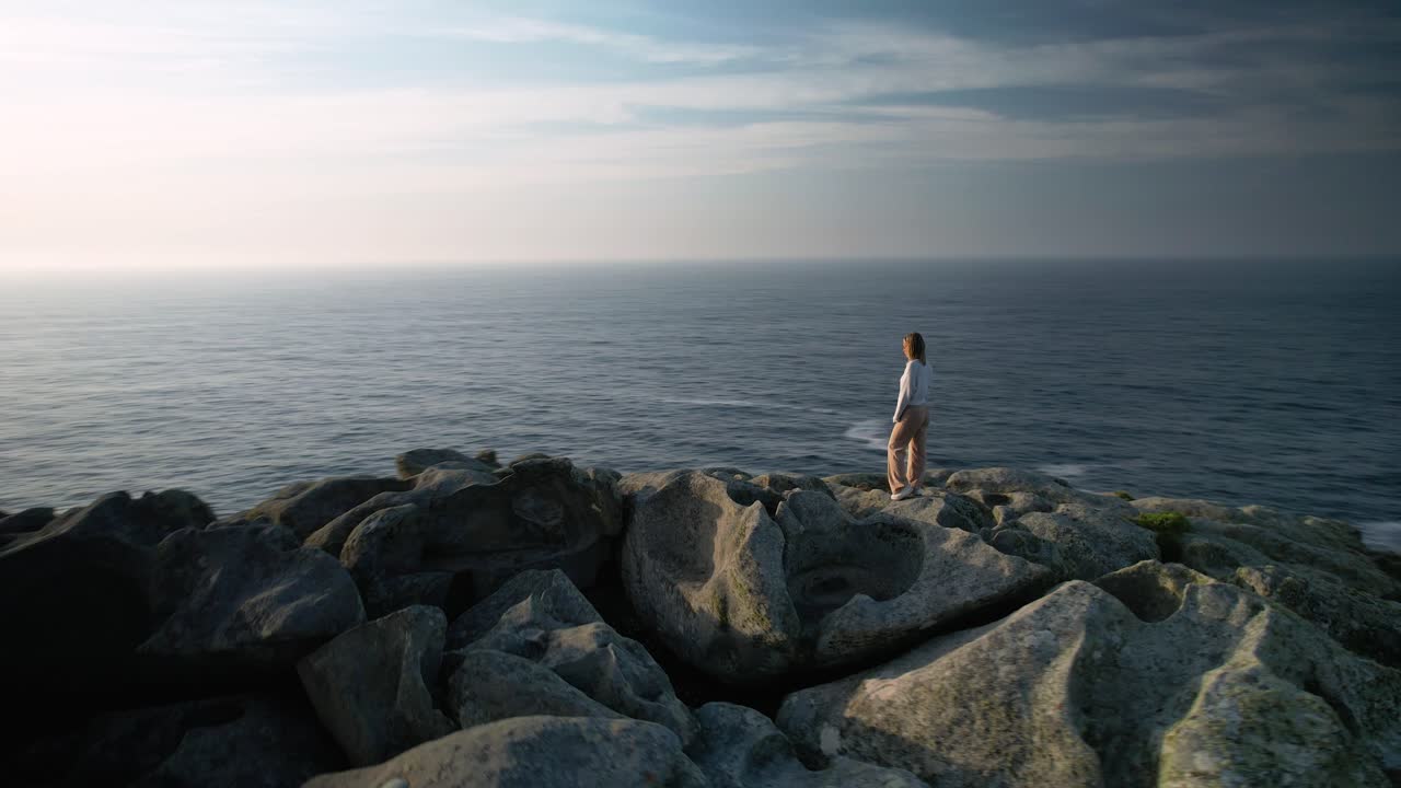 스페인 코루냐에 있는 말피카 해안의 햇빛 아래 바위에 서 있는 여성 관광객