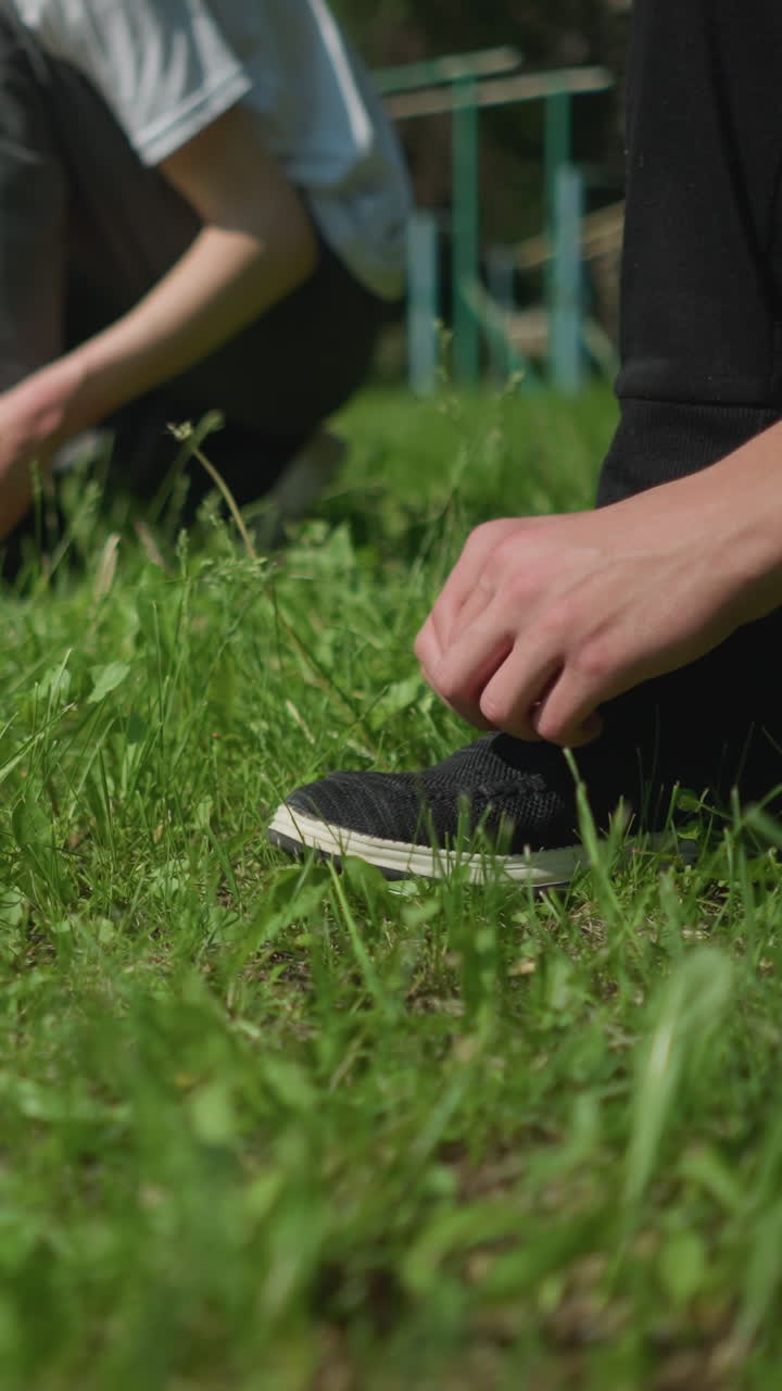 Close-up view of several people lined up on a grassy field, each kneeling down tying their shoelaces