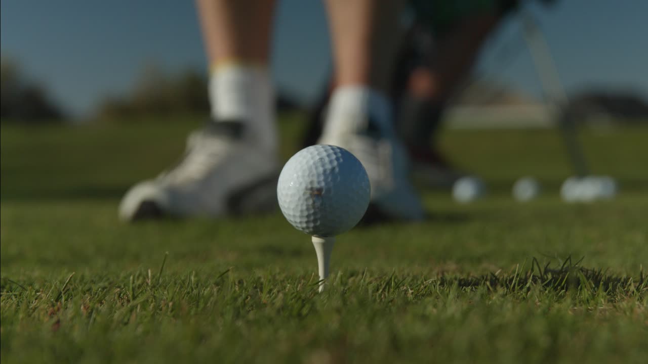 티 센터 프레임에 있는 골프공의 클로즈업과 그의 클럽으로 샷을 정렬하는 골퍼