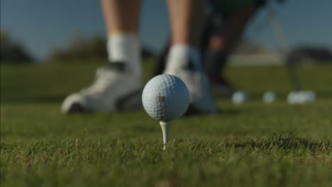 un primer plano de una pelota de golf en el marco central de un tee y el golfista alineando su golpe con su palo