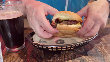 a person enjoys a burger and drink at a wooden table, capturing a casual dining experience with natural lighting