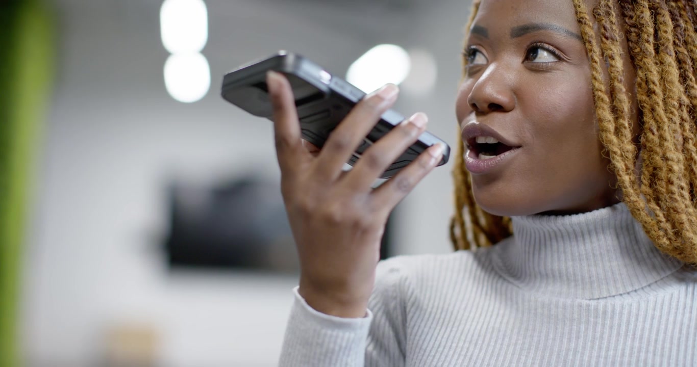 Mid-adult African American woman tapping speaker on smartphone and recording message at office
