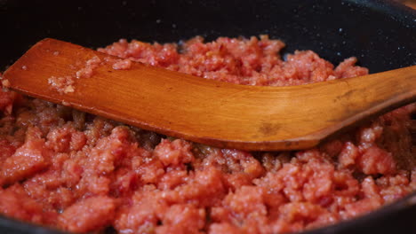 cooking meat with wooden spoon in a pan