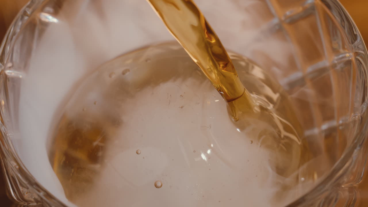 Bourbon Whiskey versato su un cubetto di ghiaccio rotondo in un bicchiere da cocktail al bar, al rallentatore