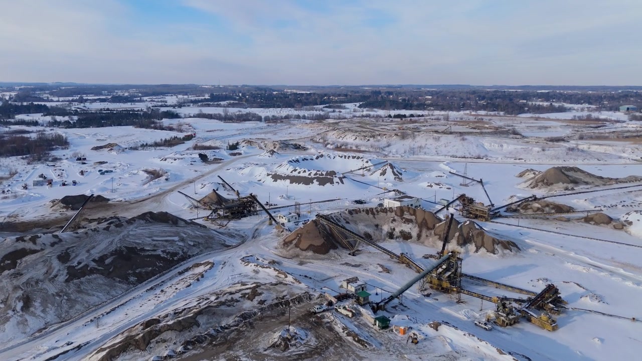 Industrial gravel pit operations in a snowy landscape with machinery visible.