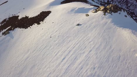 Aerial-View-of-Mountain-Ridge-With-Fresh-Powder-Pan-up-To-Valley-With-Sun-Flare-Over-Horizon