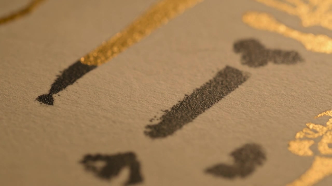 Pulling macro lens revealing textured cream paper strokes to show metallic gold and black pigment