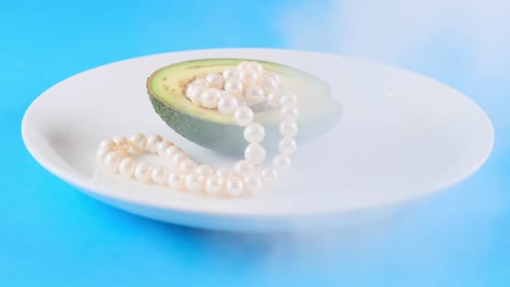 medio aguacate con perlas en una placa blanca con humo en un fondo azul. diseño de alimentos de moda