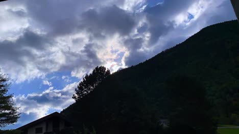 Imágenes-De-Nubes-Pesadas-En-Movimiento-Y-Montaña-Con-árboles,-Luz-Solar-En-El-Fondo-Y-Casa-En-Primer-Plano