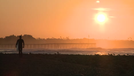 Surfer-silhouette-getting-out-of-the-water-during-sunrise-at-Surfers-Point-in-Ventura-California