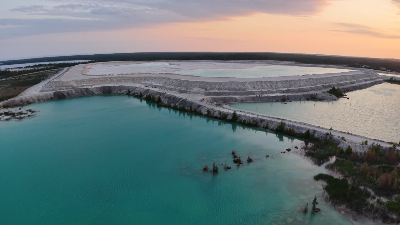 Aerial drone view of turquoise quarry lake reflecting a colorful sunset sky over rugged terrain
