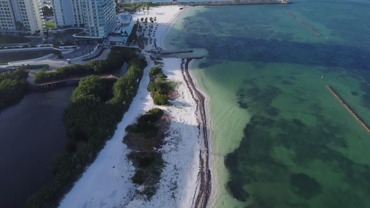 Aerial Drone View of the Cancun Coastline, tilting up to reveal hotels on the oceanfront with clear blue ocean waters