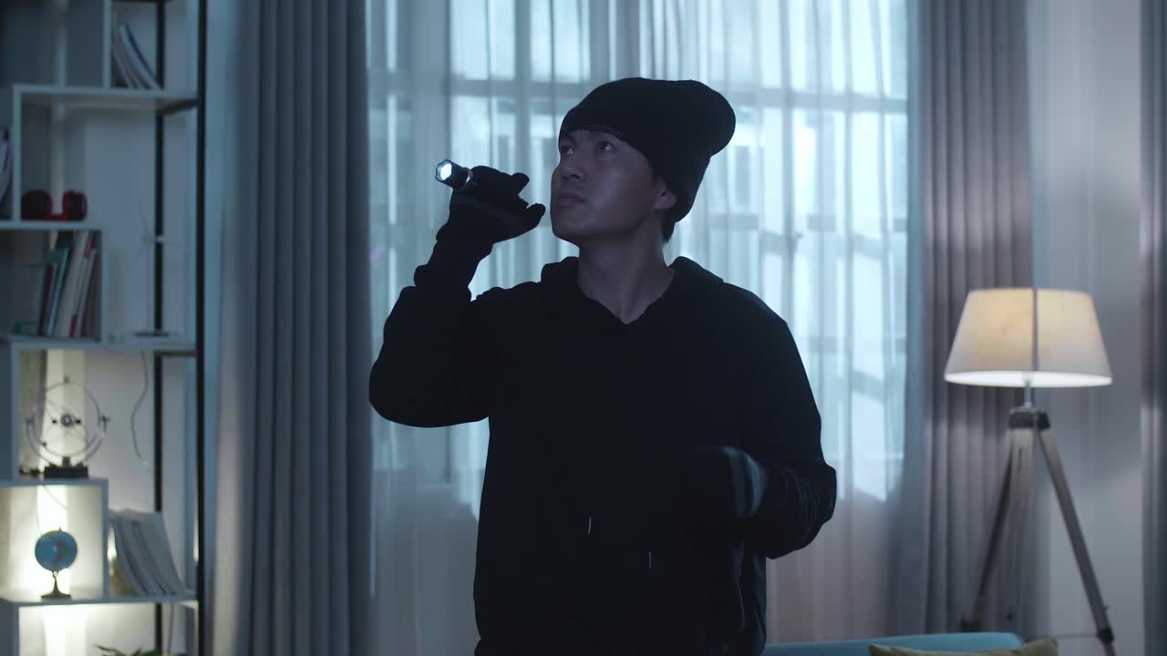 아시아인 도 남자가 불을 들고 주위를 둘러보고 누군가의 집에 걸어가는 동안 마스크를 내려놓고 있습니다.