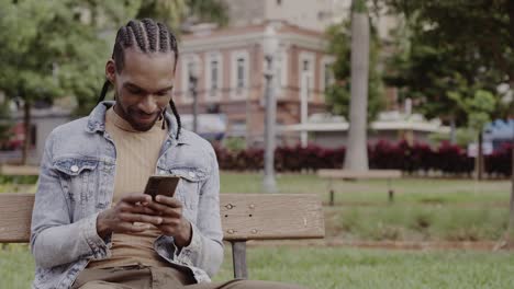 Young Man Using Smartphone While Sitting on a Park Bench