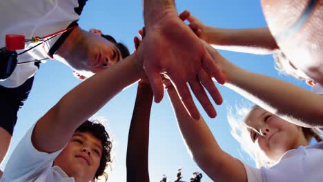 School-kids-and-coach-stacking-hands-in-campus