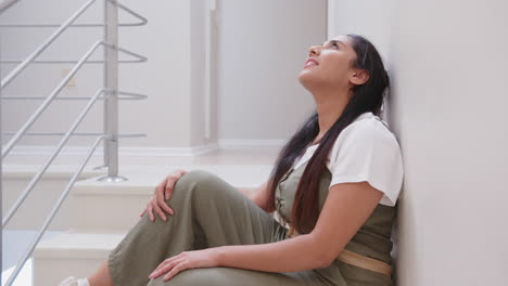 relaxing against wall, mature asian woman sitting and looking up thoughtfully, at home
