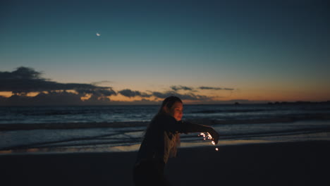 woman-playing-with-sparkler-on-beach-at-sunset-celebrating-new-years-eve-girl-having-fun-dance-waving-sparkler-firework-enjoying-celebration-by-the-sea