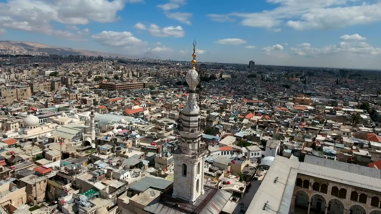 vista aérea sobre la mezquita de los umayyad en siria. un avión no tripulado está volando sobre la mesquita y el minarete con la ciudad de damasco en el fondo.