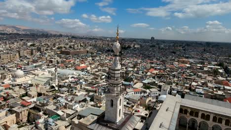 aerial view over the umayyad mosque in syria. drone is flying over the mosque and the minaret with the city of damascus in the background.