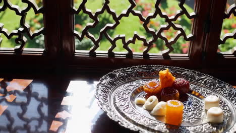 assortment of indian sweets on an ornate silver plate by a window