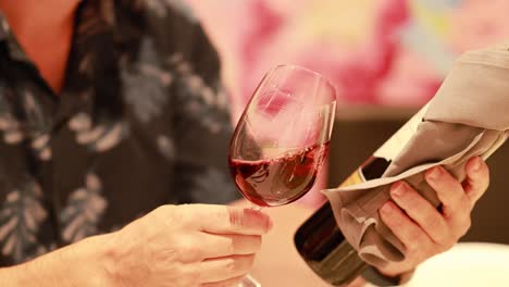 a person elegantly swirls red wine in a glass, showcasing refined dining ambiance with soft lighting and a vibrant background
