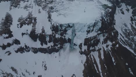 snowy iceland mountains with flowing waterfall cascading off cliff - aerial