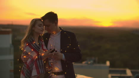 una pareja enamorada está sentada en el techo de la casa. en la distancia las luces de la ciudad nocturna.