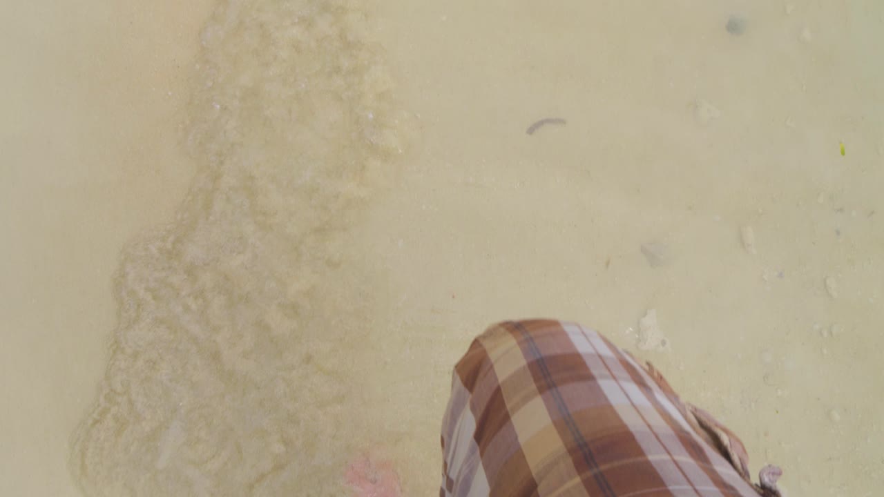 A person's legs and feet walking and splashing in shallow water