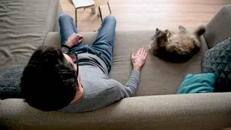 Top-View-Of-A-Blind-Man-In-Sunglasses-Sitting-On-The-Sofa-At-Home-Near-His-Cat