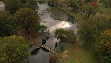 Un-Dron-Aéreo-Disparó-Sobre-Un-Parque-En-El-Día-Con-Un-Estanque,-Con-Un-Puente-Peatonal-Arqueado