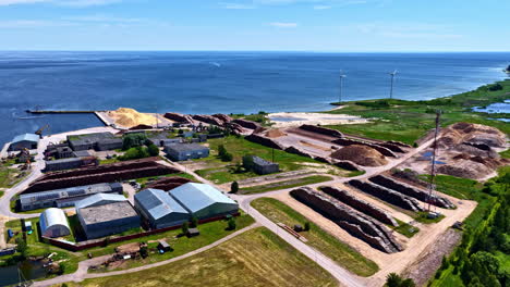 aerial view of seaside industrial site with buildings, wind turbines and log storage in latvia
