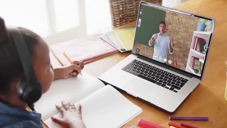 chica afroamericana usando una computadora portátil para una lección en línea con un profesor caucásico en la pantalla