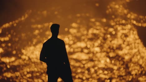 a man's silhouette stands beside the glowing rivers of lava from the pacaya volcano in guatemala - medium shot