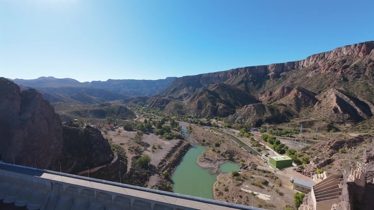 FPV aereo sopra il lago e la diga di Valle Grande, che esegue un backflip acrobatico e si tuffa verticalmente lungo l'enorme parete di cemento della diga.