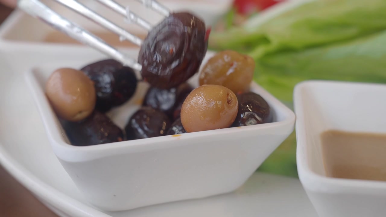 Close-up of a Fork Picking an Olive from a Bowl