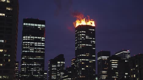 huge fire burning on top of modern skyscraper at night with other illuminated buildings in downtown business district, concept of financial crisis and economic recession