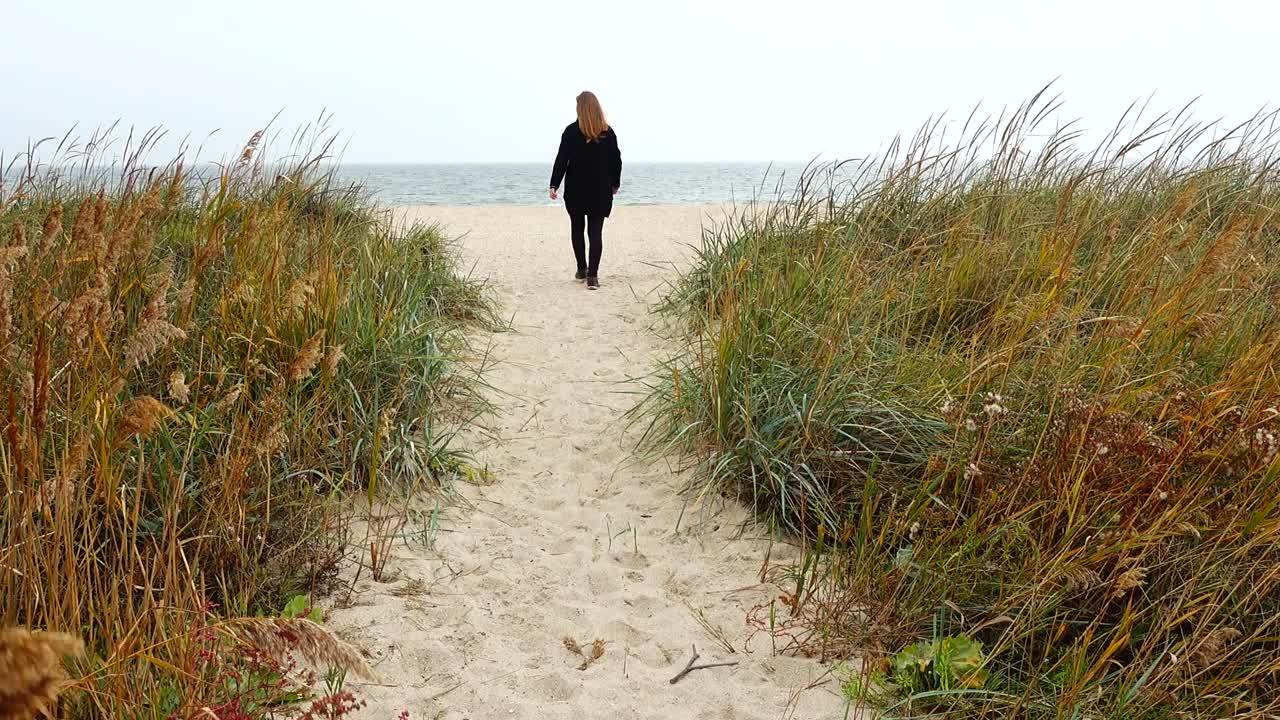 Pigen går på stranden ad en sti. Optagelse om efteråret