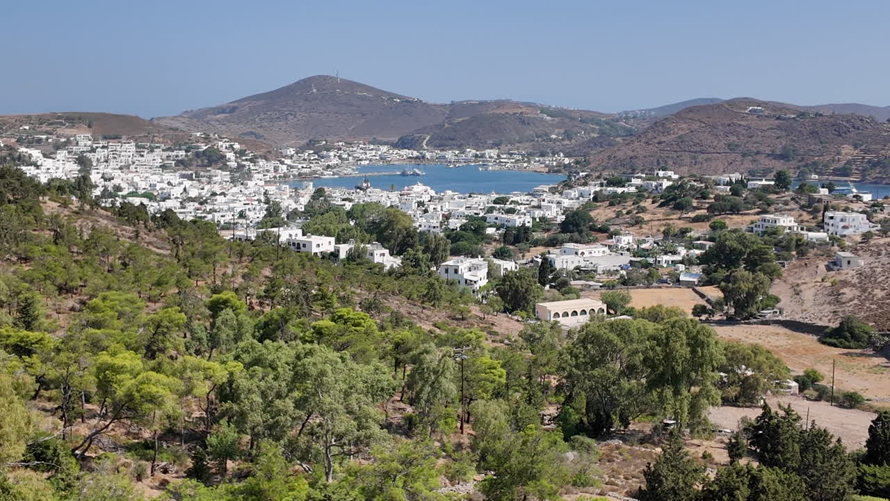 Greece, Patmos Island, Scala town view from the hill top, hills of green, traditional white houses and the Scala Bay. Picturesque island with beautiful landscapes and buildings.