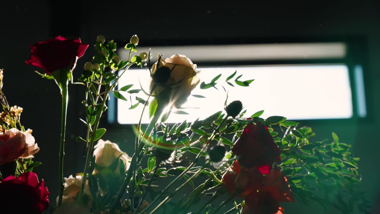 A dramatic close-up shot of floral arrangements with roses and greenery, backlit for a striking silhouette effect. Captured at a South Georgia fall wedding