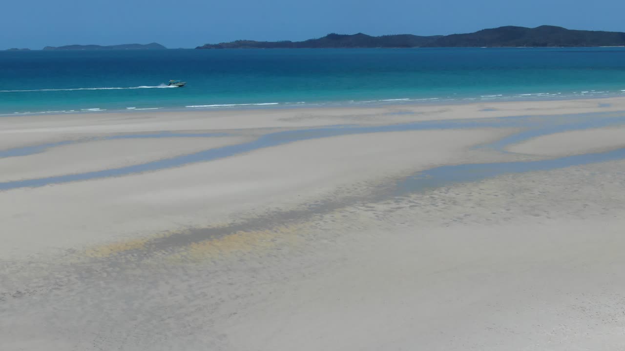 모터보트가 화이트 헤이븐 해변 해안에서 떨어진 푸른 바다를 가로질러 드론 공중 추적 샷을 찍습니다.