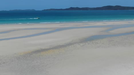 Una-Lancha-Corta-A-Través-De-Las-Aguas-Azules-Del-Océano-Frente-A-La-Costa-De-La-Playa-De-White-Haven,-Tiro-De-Seguimiento-Aéreo-De-Drones