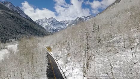 aerial panning shot of a remote road in the middle of the maroon bells aspen mountain range during winter in colorado