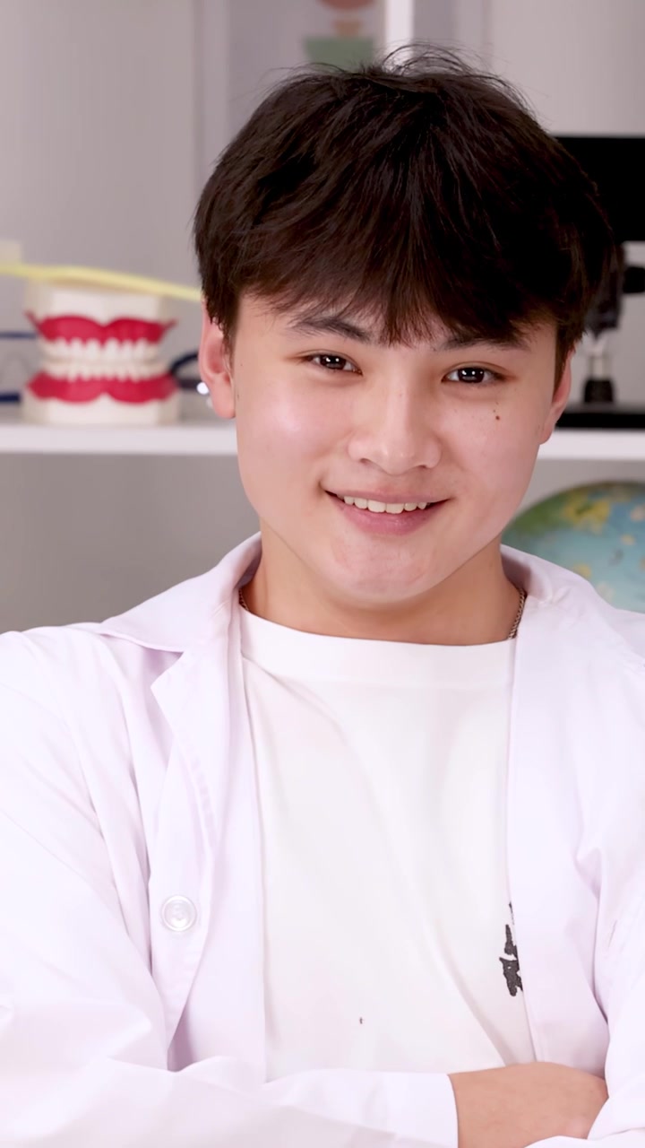 Confident student in white lab coat smiles at camera in bright science laboratory setting.