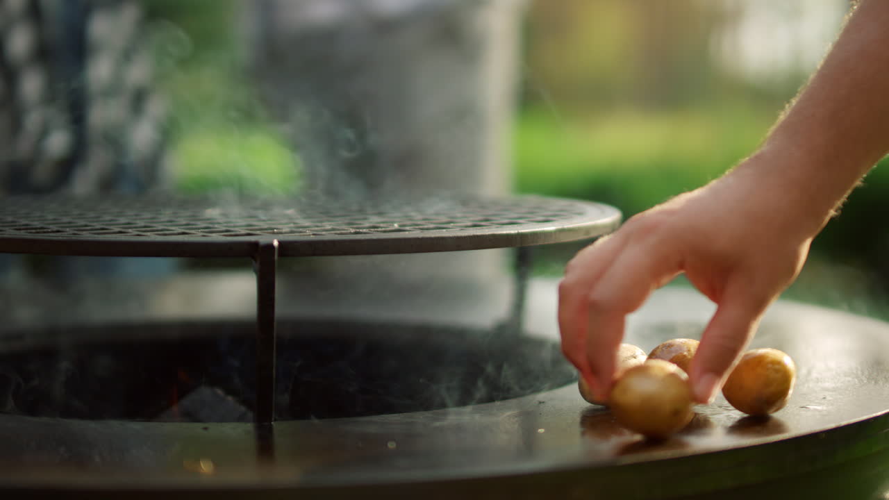 Cuoco che prepara patate su una griglia barbecue all'aperto. Un uomo mette le patate sulla griglia.