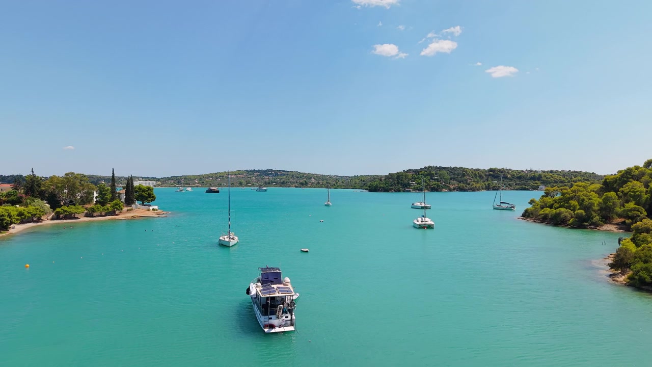 Il drone vola in avanti sopra la splendida baia turchese di Porto Cheli in estate. Barche a vela e yacht navigano placidamente tra lussureggianti penisole verdi sotto un sole splendente di mezzogiorno