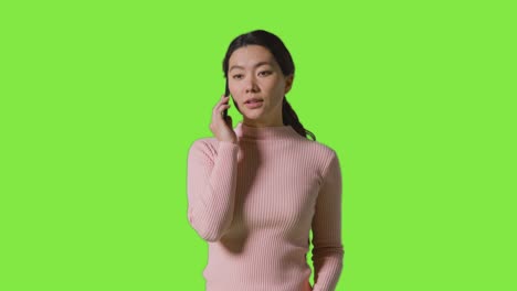 studio shot of woman answering mobile phone and getting bad news against green screen