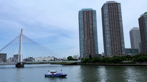 Skyscrapers-line-the-riverbank-under-a-clear-sky,-reflecting-in-the-calm-water